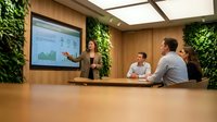 Professional businesswoman presenting financial data on screen to diverse team in modern eco-friendly conference room with living green walls and natural lighting.
