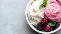 Creamy vanilla and raspberry ice cream scoops in white bowl garnished with fresh blackberries, raspberries and mint leaves on marble background.
