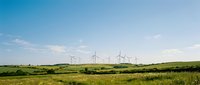 Wind turbines stand across rolling green hills under a bright blue sky with scattered clouds, representing renewable energy and sustainable power generation for environmental and industrial projects.