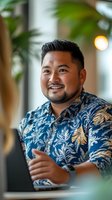 Confident Asian businessman in tropical print shirt smiling at modern office workspace with laptop and plants for professional lifestyle content.