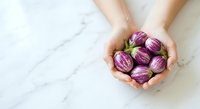 Fresh purple eggplants held in hands over marble surface, suitable for food, cooking, recipe, and culinary design projects.