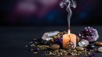 Burning candle with pentagram symbol surrounded by crystals, herbs and mystical elements for spiritual rituals and esoteric practices.