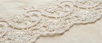 Delicate cream lace trim with ornate floral and scrollwork patterns on neutral background, suitable for wedding invitations, textile design, and craft projects.