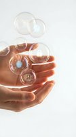 Cupped hands releasing floating transparent bubbles with digital icons representing technology concepts and innovation on clean white background.