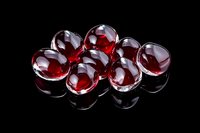 Red transparent glass marbles arranged in group on black reflective surface with dramatic lighting creating glossy highlights and deep shadows.