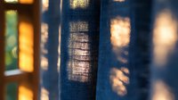 Close-up of blue denim fabric with warm golden sunlight filtering through, creating soft shadows and highlights on textured cotton material.