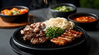 Steaming hot grilled meat platter with noodles and fresh herbs served on black plate, accompanied by spicy sauces and side dishes in dark setting.