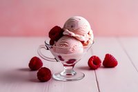 Creamy raspberry ice cream scoops in elegant glass bowl with fresh berries on pink background, perfect for dessert menu photography.