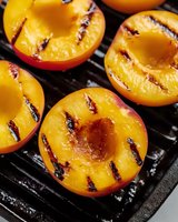 Fresh halved peaches with grill marks on cast iron grating, showing juicy golden flesh and charred lines from grilling. Close up macro food photography.