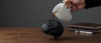 Person pouring coffee into a brain model on wooden desk with notebook and pen, representing mental stimulation, creativity, and cognitive enhancement for business concepts.
