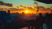 Silhouette of person relaxing on balcony with panoramic city skyline view during golden sunset, enjoying peaceful evening atmosphere.