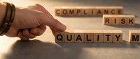 Male hand with wristband arranging wooden blocks spelling compliance, risk, and quality management concepts for business strategy and regulatory standards.