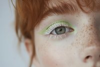 Close-up of a freckled redhead woman with green eyes and bold lime green eyeliner with white lashes, creative makeup art.