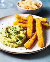 Crispy polenta fries with creamy avocado dip and macaroni cheese, served on white plate against blue background for food blog or recipe website.