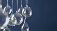 Clear glass Christmas ornaments hanging on silver strings against dark blue background for holiday decorations and festive seasonal displays.