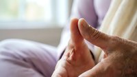 Senior man massaging his foot while sitting on bed, elderly healthcare and pain relief concept for arthritis or plantar fasciitis treatment at home.
