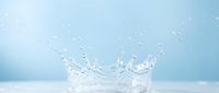 Water splash with droplets frozen in motion against soft blue background, suitable for beverage, wellness, and product advertising campaigns.