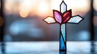 Stained glass cross with pink, blue and white petals against blurred bokeh background, spiritual symbol illuminated by soft light creating peaceful atmosphere.