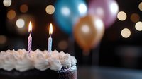 Chocolate cupcake with lit birthday candles and whipped cream frosting against blurred background with colorful party balloons and festive bokeh lights.