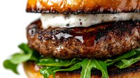Juicy grilled beef burger with melted cheese, fresh arugula and caramelized brioche bun in macro shot showing texture and layers for restaurant menu and food advertising.