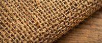 Natural burlap fabric texture with woven jute fibers on rustic wooden surface for craft projects and rustic decor applications.