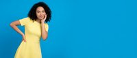 Young African American woman in yellow dress posing confidently against bright blue background with copy space for advertising and marketing campaigns.
