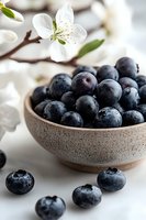 Fresh blueberries in ceramic bowl with white cherry blossom flowers in background. Healthy organic berries with water drops on light surface.