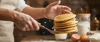 Chef flipping golden pancakes with spatula in rustic kitchen. Cooking breakfast, homemade food preparation, culinary skills demonstration.