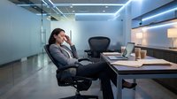 Stressed businesswoman sitting at office desk with head in hands showing workplace burnout and mental fatigue in modern corporate environment.
