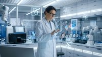 Asian male scientist in white lab coat using digital interface technology in modern research laboratory with robotic equipment and holographic displays.