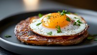 Sunny side up egg on crispy hash brown potato pancake garnished with fresh herbs and black pepper served on dark plate, close up view of breakfast dish.