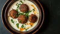 Homemade meatballs in creamy white sauce with fresh herbs served in rustic ceramic bowl. Traditional comfort food recipe for family dinner and cooking blogs.
