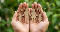 Wooden family figures held in protective cupped hands against green nature background symbolizing care, support and family protection concepts.