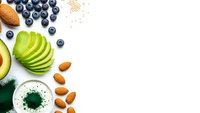 Fresh healthy breakfast ingredients with sliced avocado, blueberries, almonds and green smoothie on white background for nutrition concept.