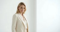 Professional blonde businesswoman in elegant beige suit standing confidently in modern office interior with natural lighting for corporate presentations.