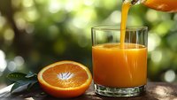 Fresh orange juice being poured into glass with orange half on wooden table outdoors for healthy breakfast and natural vitamin C drink concept.