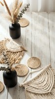 Boho home decor with woven jute placemats, pampas grass in black vases and eucalyptus on rustic white wooden floor for interior design projects.