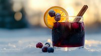 Mulled wine with orange slice and cinnamon stick in glass, garnished with cranberries on snowy surface during golden hour for holiday celebrations.