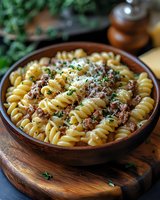 Rotini pasta with ground beef meat sauce and grated parmesan cheese garnished with fresh herbs in rustic ceramic bowl on wooden board, comfort food styling.
