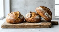 Freshly baked artisan sourdough bread loaves on rustic wooden cutting board in modern kitchen setting for bakery and food photography.
