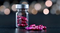 Pink medical capsules spilling from glass vial on dark surface with soft bokeh lights in background, pharmaceutical and healthcare concept.