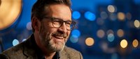 Smiling mature Caucasian businessman with glasses and beard in elegant suit against blurred city lights background for corporate presentations.