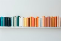 Colorful books arranged in rainbow gradient order on white shelf against light wall, creating minimalist aesthetic composition for home decor and interior design.