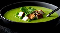 Creamy green pea soup garnished with crispy croutons, fresh mint leaves and pumpkin seeds served in black bowl on dark background. Food photography.