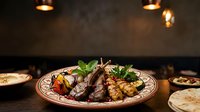 Grilled lamb chops with roasted vegetables and fresh herbs served on decorative plate in upscale restaurant setting with warm ambient lighting.
