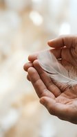Gentle hands holding delicate white feather symbolizing peace, hope, spirituality and freedom with soft natural bokeh background for mindfulness concepts.