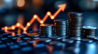 Growing stacks of silver coins with glowing orange arrow trending upward on laptop keyboard, representing financial growth and investment success.