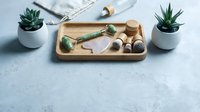 Spa and wellness flat lay with wooden tray holding natural skincare tools, jade roller, wooden spoons, and succulent plants on marble surface for beauty and relaxation content.
