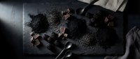 Dark chocolate pieces with cocoa powder and blackberries on slate board creating moody culinary composition for gourmet dessert photography.