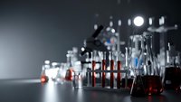 Laboratory glassware with red liquid samples in test tubes and beakers on dark surface with blurred background lights for scientific research and analysis.